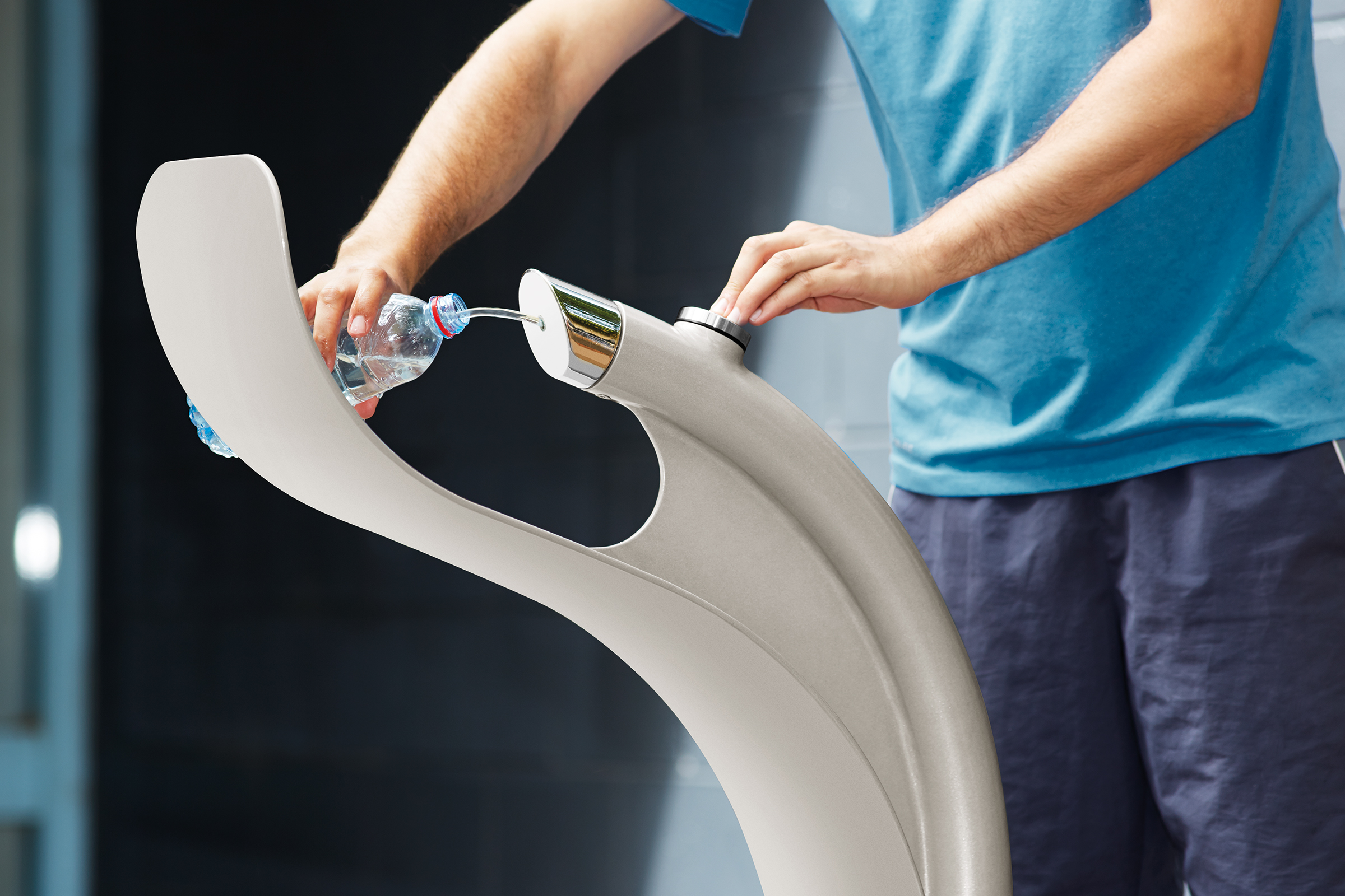 Person in a blue shirt pours water from a bottle into a built-in water dispenser on a modern fitness machine.