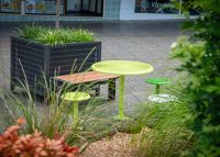 Frame Planters (PT3, Square XL) with Slots perforation in Textura Monument, height-adjustable legs. Aria Bench in aluminium Spotted Gum. Cafe Settings in Lycra Strip Green, Viper Green and Pearl White.