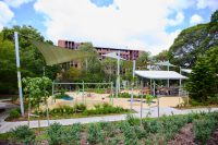 Johnson Park. Children's playground with climbing structures and rubberized surface under green shade sails in a sunny park area.