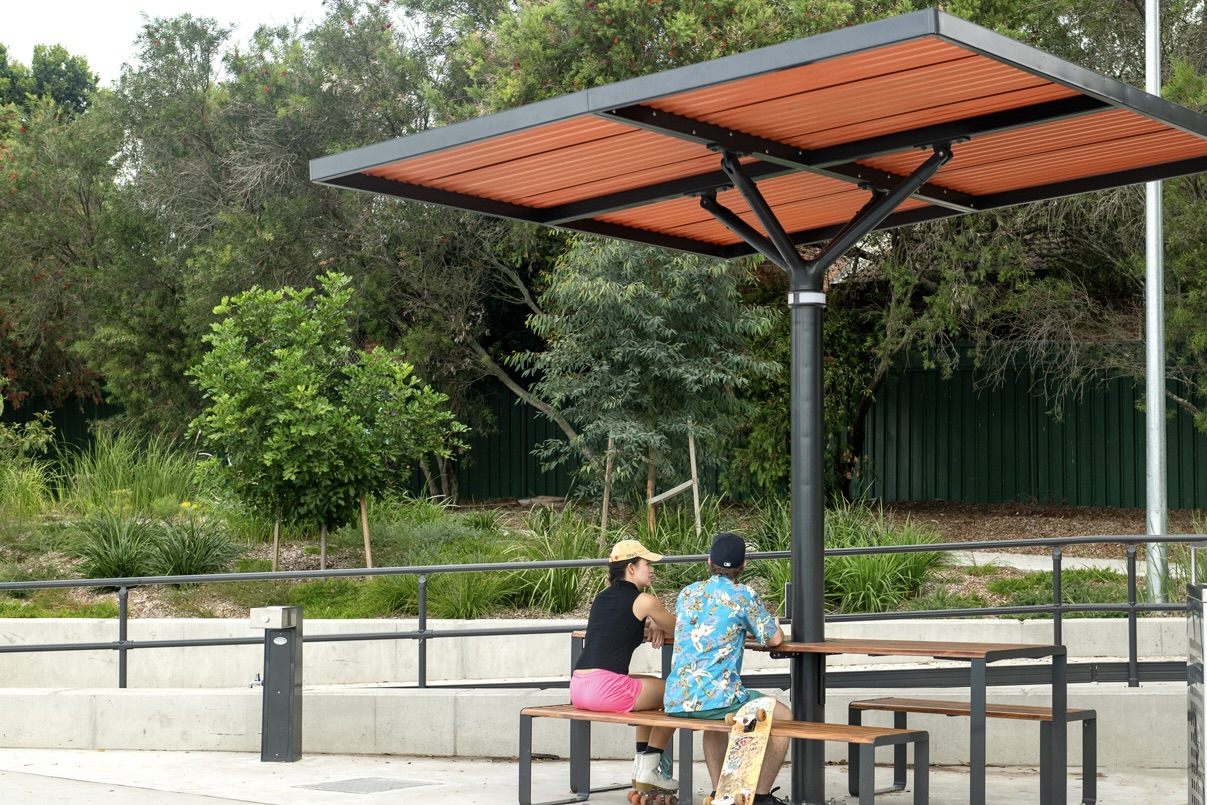 Olds-Park_Street-Furniture-Australia_0-1 - Street Furniture Australia ChillOUT Tree (CT1) powered, in Satin Monument with custom roof colour (Red Dust). Linea Table (LIT10-DDA) and Linea Bench (LIB6) in aluminium woodgrain Spotted Gum battens and Textura Monument frame.