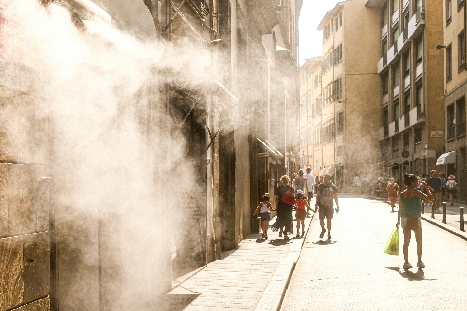 Summer street scene in Firenze, Italy, during a heat wave. People walking under the strong Tuscan sunlight with refreshing water mist in the urban atmosphere.
