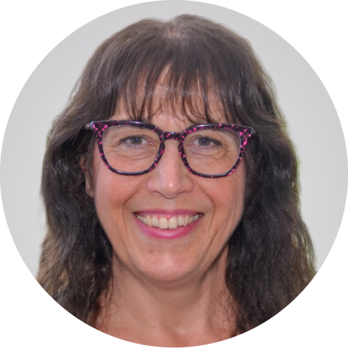 Portrait of a smiling woman with dark hair and pink-framed glasses facing the camera, against a neutral background.